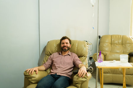 Cheerful happy man smiling making eye contact while getting IV drip therapy at the wellness clinic for a vitamins cocktail for better healthの写真素材