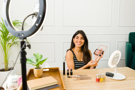 Smiling woman showcases cosmetics during an online tutorial with ring light and cameraの写真素材