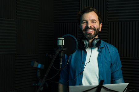 Cheerful man with headphones recording audio in a professional sound boothの写真素材