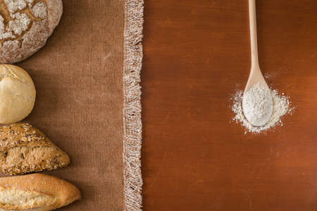 Composition of various breads on a tablecloth with edges of white threads on brown wooden tableの写真素材