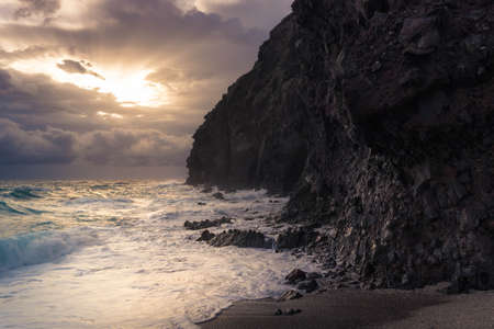 After a long stormy night with heavy rain and wind, it dawns on the beaches of the province of Almeria, showing the first rays of sun and a rough sea crashing against the rocks of the cliffs.の写真素材