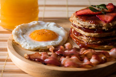American breakfast consisting of an egg, a few slices of bacon and a pancake of strawberry jam and strawberries. Drink a natural orange juice.の写真素材