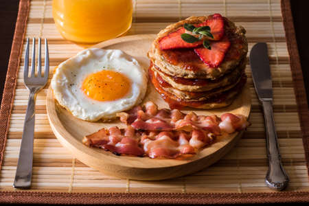 American breakfast consisting of an egg, a few slices of bacon and a pancake of strawberry jam and strawberries. Drink a natural orange juice.の写真素材