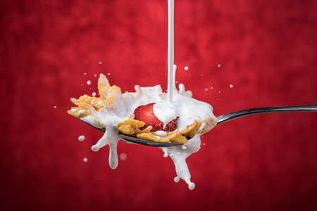 Milk falling on a cereal spoon with strawberry