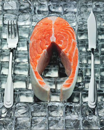Fresh steak of fish on ice with metal fork and knifeの写真素材