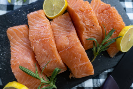 Raw salmon fillets with lemon and rosemary on black slate plateの写真素材