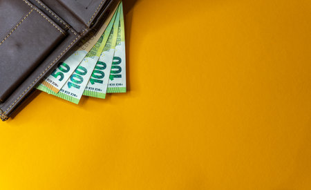 Money in a brown leather wallet on a yellow background. Copy space