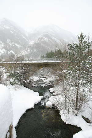 Stone bridge over a river in a snowy and foggy mountainの写真素材