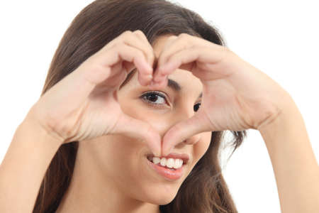 Beautiful woman making a heart shape with her hands and watching through it on a white isolated backgroundの写真素材