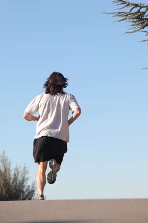 Back view of a man running on a road with the sky in the backgroundの写真素材