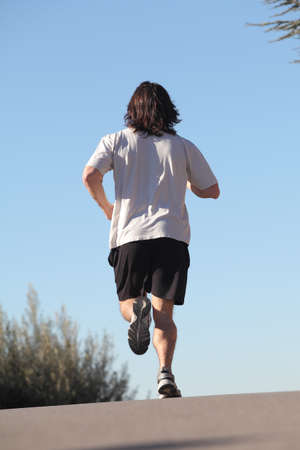Back view of a man running on a road with the sky in the backgroundの写真素材