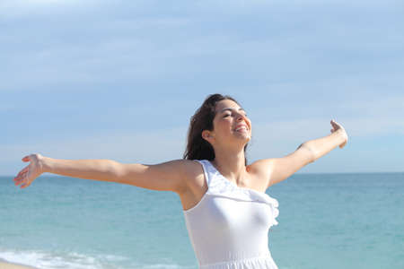 Beautiful girl with her arms raised on the beach with the sea in the backgroundの写真素材