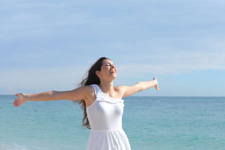 Happy beautiful girl with her arms raised on the beach with the sea in the backgroundの写真素材