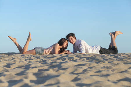 Couple laughing resting on the sand of a beach with the sky in the backgroundの写真素材