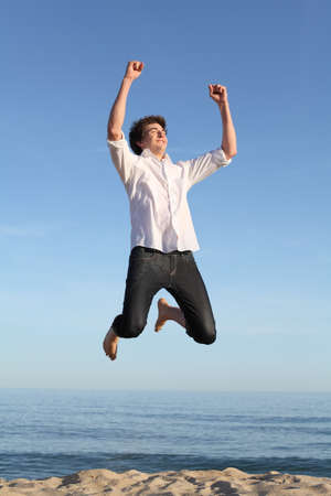 Boy jumping happy on the beach with the sea and a blue sky in the backgroundの写真素材