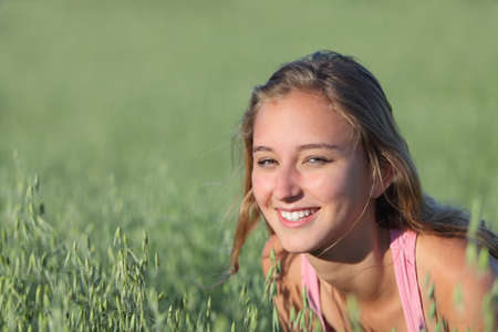 Portrait of a beautiful teenager girl smiling in an unfocused green oat meadowの写真素材