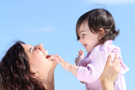 Attractive mother raising her daughter and playing together with the blue sky in the backgroundの写真素材