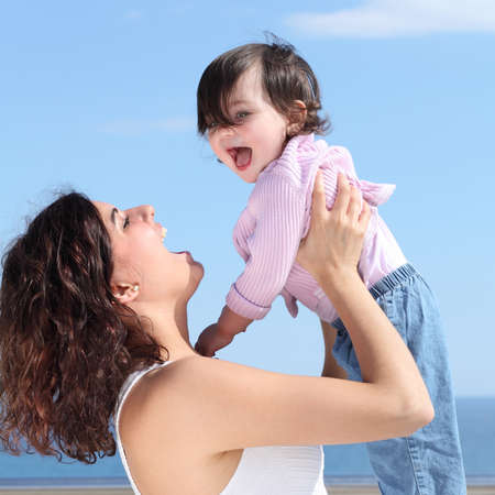 Pretty mum laughing and raising her daughter with the blue sky in the backgroundの写真素材