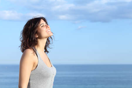 Beautiful girl breathing and smiling on the beach with the sea and blue sky in the backgroundの写真素材