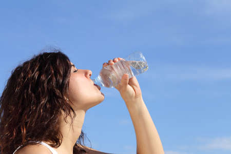 Profile of a woman drinking water from a plastic bottle with a blue sky in the backgroundの写真素材