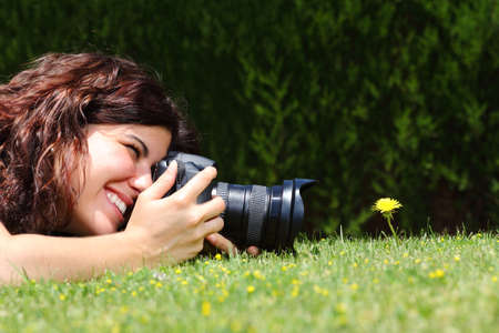 Profile of a beautiful woman taking a macro photography of a flower on the grass in a parkの写真素材