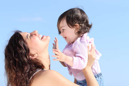 Attractive mum raising her daughter and playing together with the blue sky in the backgroundの写真素材