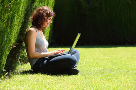Pretty woman sitting on the grass in a park working with her laptop       の写真素材