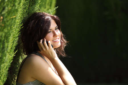 Beautiful woman talking on the mobile phone in a park with a dark background         の写真素材