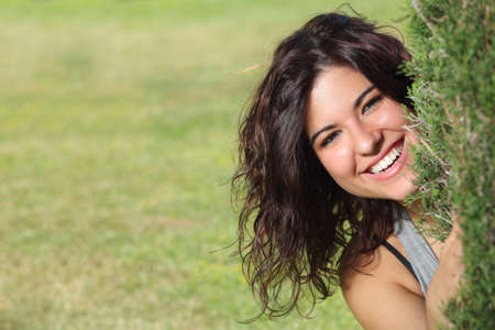 Beautiful woman peeking through a tree and smiling with a green grass backgroundの写真素材