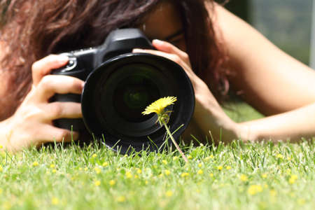 Close up of a pretty girl taking a photograph of a flower on the grass in a parkの写真素材