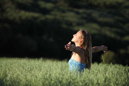 Attractive woman breathing joyful with raised arms in a green meadow with a dark backgroundの写真素材