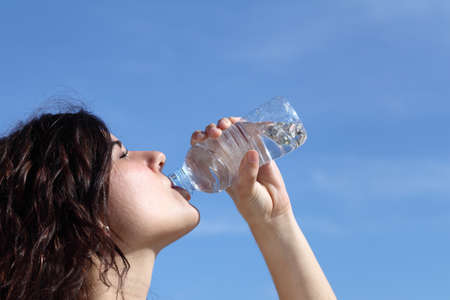 Profile of a beautiful woman drinking water from a plastic bottle with a blue sky in the background           の写真素材