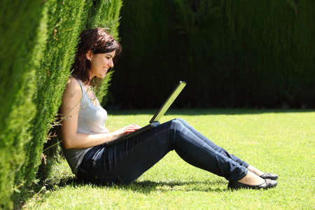 Attractive woman happy in a park working with her laptop with an unfocused dark background  の写真素材