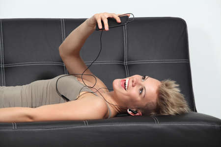 Profile of a woman at home lying on a couch listening to the music from a smartphone               の写真素材