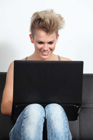 Fashion teenager girl at home sitting on a couch browsing in a laptop の写真素材