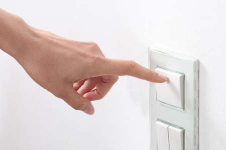 Woman hand turning on the light with a wall switch
