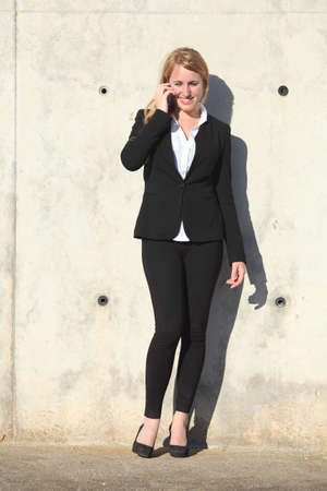 Businesswoman talking on the phone leaning on a concrete wallの写真素材