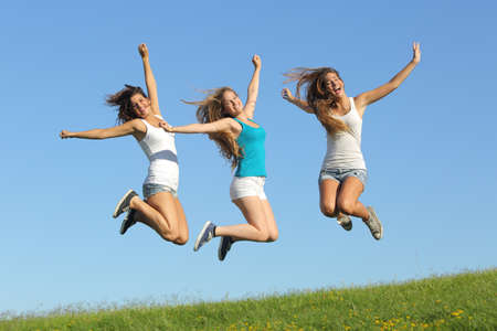 Group of three teenager girls jumping on the grass with the blue sky in the background                の写真素材