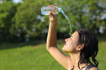 Beautiful woman throwing herself water from a bottle with a green backgroundの写真素材