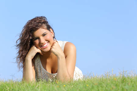 Portrait of an attractive woman lying on the grass with a blue sky in the background            の写真素材