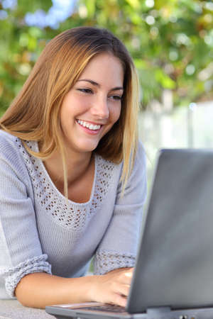 Beautiful woman happy browsing internet in her laptop outdoor          の写真素材