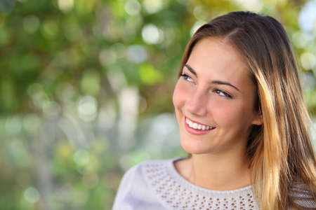 Beautiful pensive woman smiling looking above outdoor with a green unfocused background             の写真素材