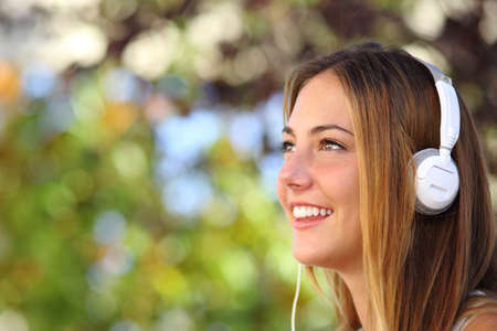 Profile of a beautiful woman listening to the music with headphones outdoor with a green background      の写真素材
