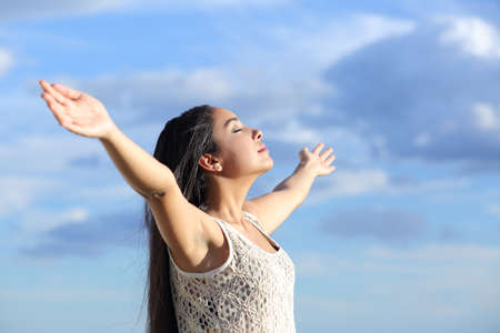 Beautiful arab woman breathing fresh air with raised arms with a cloudy blue sky の写真素材