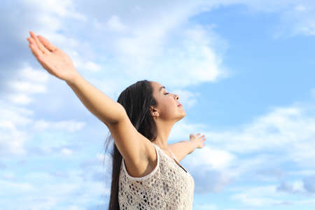 Portrait of a beautiful arab woman breathing fresh air with raised arms with a cloudy blue sky in the background         の写真素材