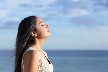Profile of a beautiful arab woman breathing fresh air in the beach with a cloudy blue sky in the backgroundの写真素材