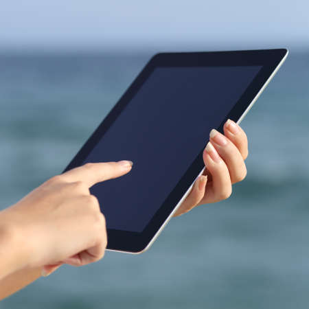 Close up of a woman hands holding and browsing a digital tablet on the beach with the sea in the background             の写真素材