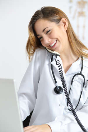 Beautiful doctor in a consultation talking on the phone and browsing in a laptop            の写真素材