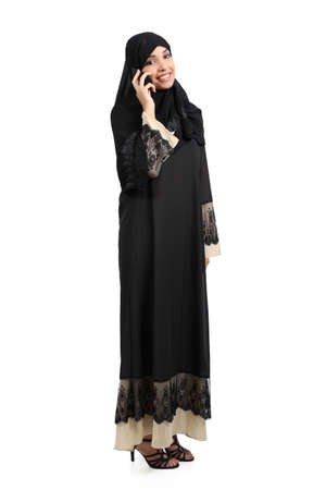 Standing arab woman talking on the phone isolated on a white background      の写真素材