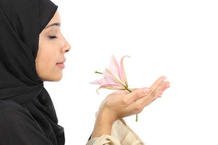 Side view of an arab woman wearing a hijab smelling a flower isolated on a white backgroundの写真素材